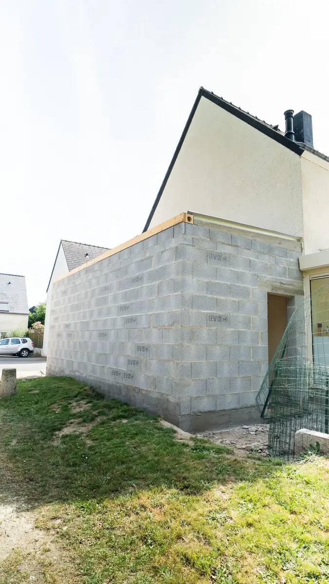 Extension en parpaing vue de côté depuis la pelouse, murs montés d'aplomb