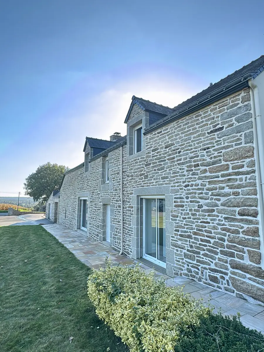 Longue façade de longère en pierre aux joints refaits, vue depuis la pelouse